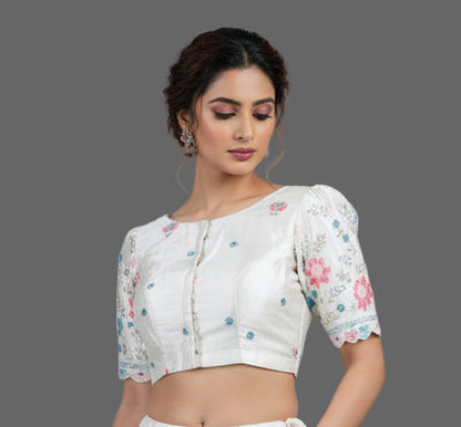 A white silk embroidered blouse with floral patterns and half sleeves displayed against a dark background.